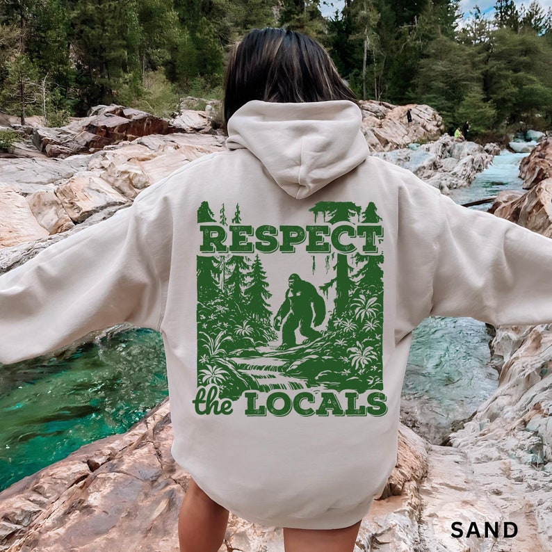 May include: A beige hoodie with a green graphic print of a Bigfoot in a forest setting. The graphic includes the text "RESPECT the LOCALS".