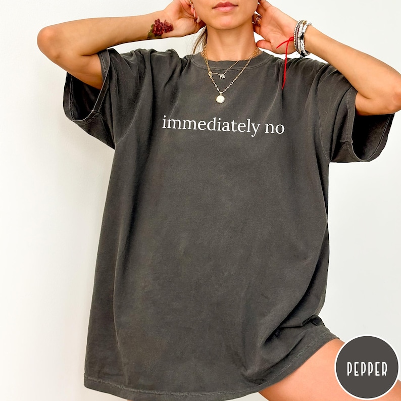 May include: Dark gray t-shirt with the phrase "immediately no" in white block letters. The shirt has short sleeves and a relaxed fit. The word "pepper" is in a circle at the bottom right.