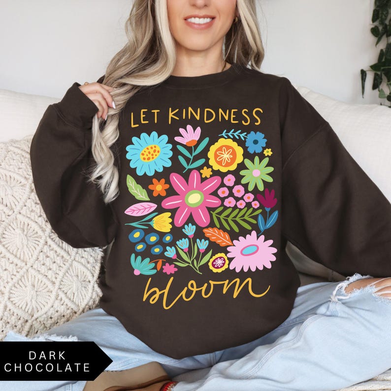 May include: A dark chocolate brown sweatshirt with a colorful floral design and the text "Let Kindness Bloom" in yellow.