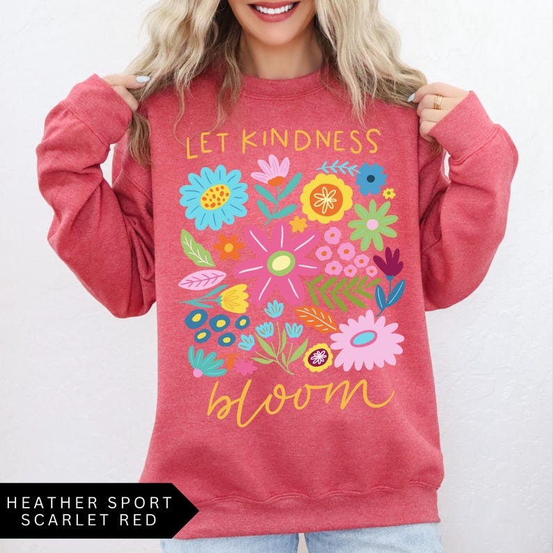 May include: A red heather sport sweatshirt with the text "Let Kindness Bloom" in white and yellow lettering. The text is surrounded by a colorful floral design.