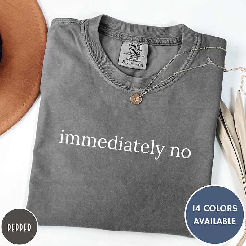 May include: A gray Comfort Colors t-shirt with the words "immediately no" in white. A silver necklace with a pendant is draped on the shirt. A circular graphic indicates "14 COLORS AVAILABLE".