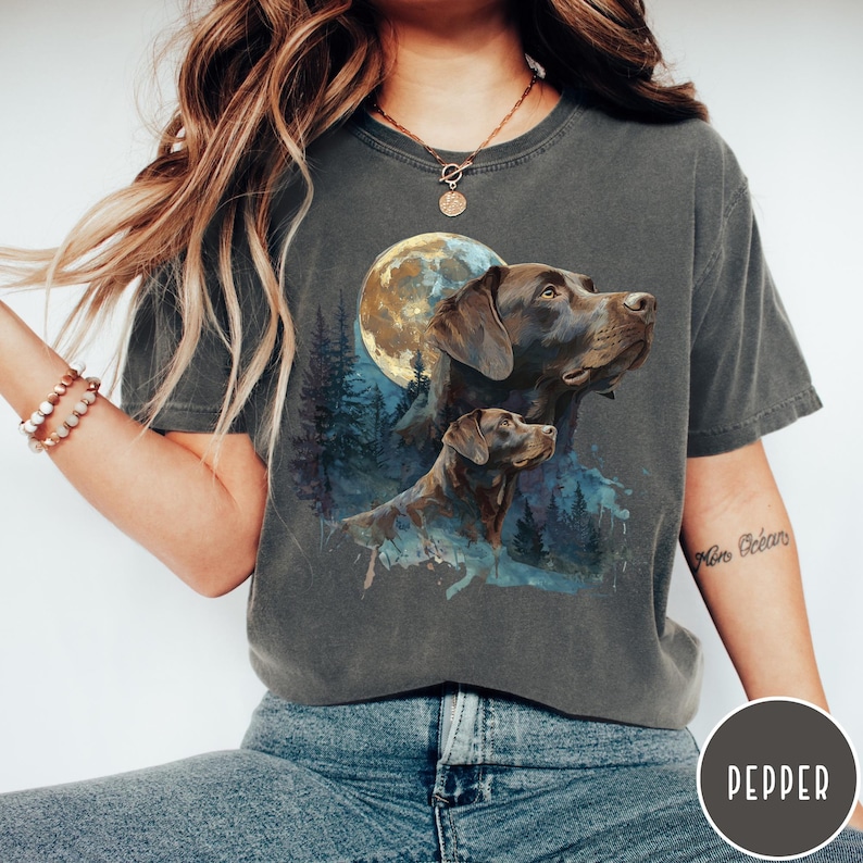 May include: Dark grey t-shirt featuring a watercolor illustration of two brown Labrador Retrievers under a full moon. The design includes a forest scene with blue and green hues. The shirt is a comfortable, casual style.