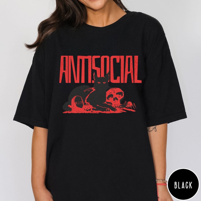 Może przedstawiać: Czarny T-shirt z czerwonym nadrukiem czarnego kota siedzącego na czaszce z napisem "ANTISOCIAL" w czerwonych literach nad nim.