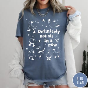 May include: A blue t-shirt with a white graphic of ducks and stars. The text on the shirt reads "Definitely not all in a row".