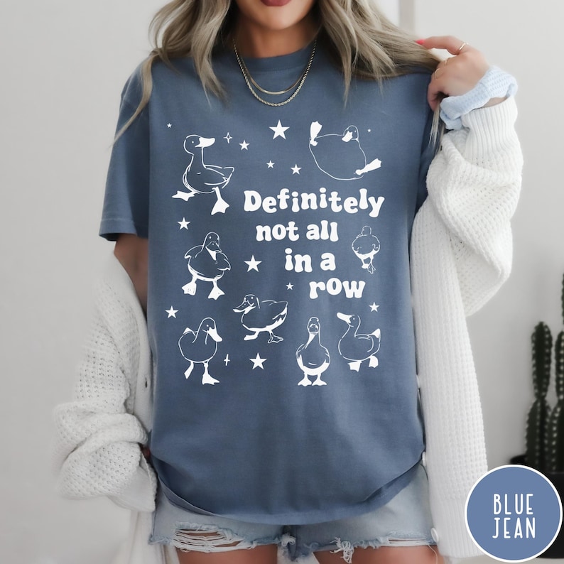 May include: A blue t-shirt with a white graphic of ducks and stars. The text on the shirt reads "Definitely not all in a row".