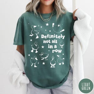 May include: A teal green t-shirt with a white graphic of ducks and the text "Definitely not all in a row".