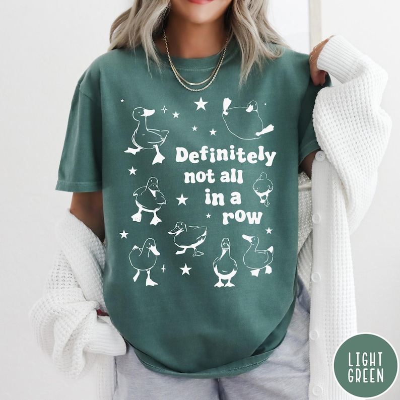 May include: A teal green t-shirt with a white graphic of ducks and the text "Definitely not all in a row".
