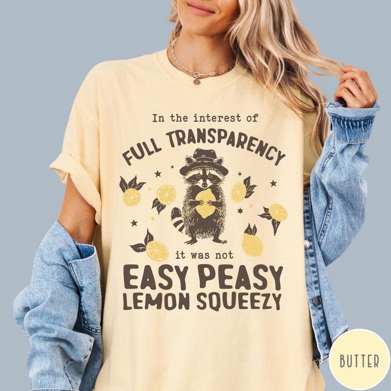 May include: A light yellow t-shirt with a raccoon holding a lemon and the text "In the interest of FULL TRANSPARENCY it was not EASY PEASY LEMON SQUEEZY".
