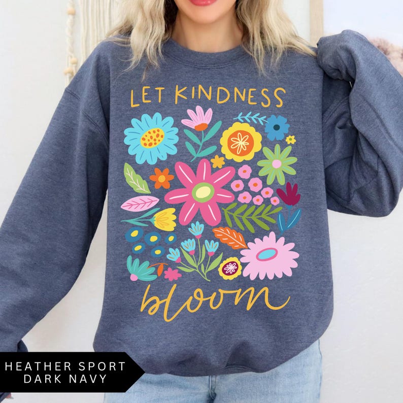 May include: A dark navy blue sweatshirt with the text "Let Kindness Bloom" in yellow and a colorful floral design.