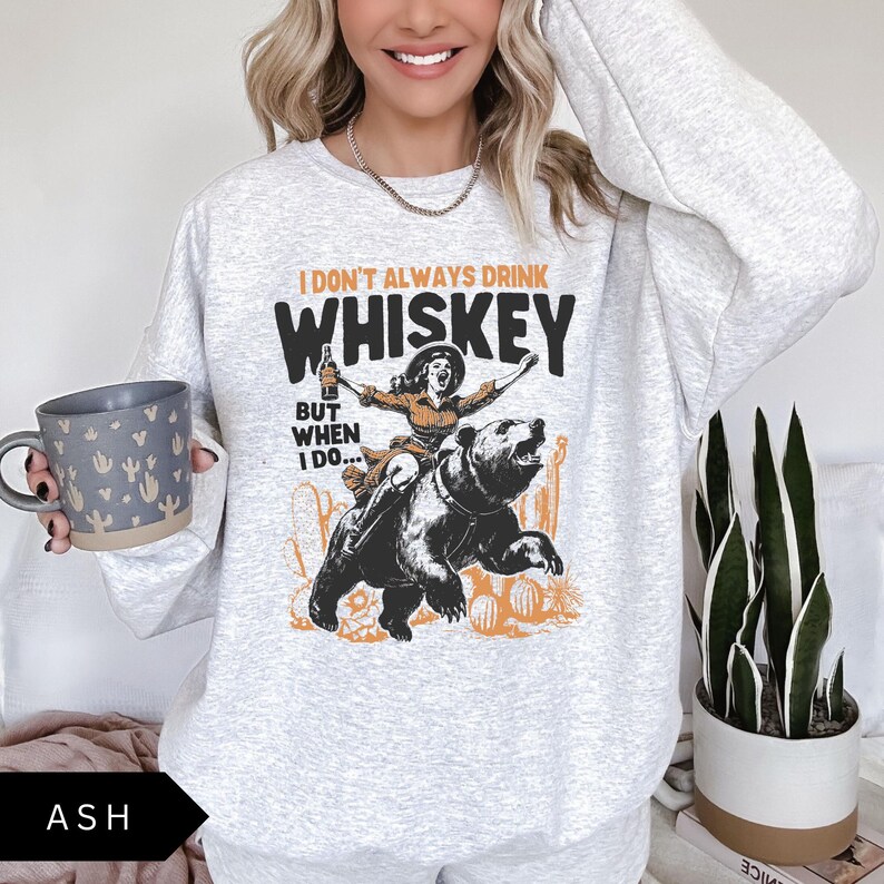 May include: A gray sweatshirt with a graphic print of a woman riding a bear. The text on the graphic reads "I don't always drink whiskey but when I do..."