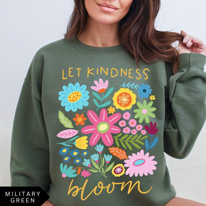 May include: A green sweatshirt with the text "Let Kindness Bloom" in yellow and white lettering. The text is surrounded by a colorful floral design with pink, blue, yellow, orange, and green flowers.