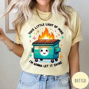 May include: A yellow t-shirt with a graphic of a green dumpster on fire with the text "This little light of mine I'm gonna let it shine".