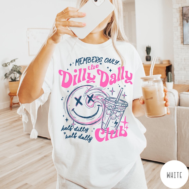May include: White t-shirt with a graphic design featuring a smiling face, a beverage, and the words "Members Only, the Dilly Dally Club." The design is in pink and blue. The shirt is a casual, everyday wear item.