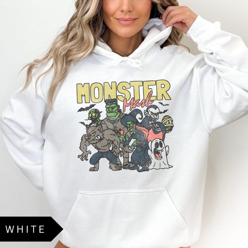 Puede incluir: Sudadera con capucha blanca con un estampado gr&aacute;fico de un grupo de monstruos de dibujos animados, incluyendo un hombre lobo, un vampiro, un fantasma y un monstruo de Frankenstein. El texto "Monster Mash" est&aacute; impreso sobre el gr&aacute;fico.