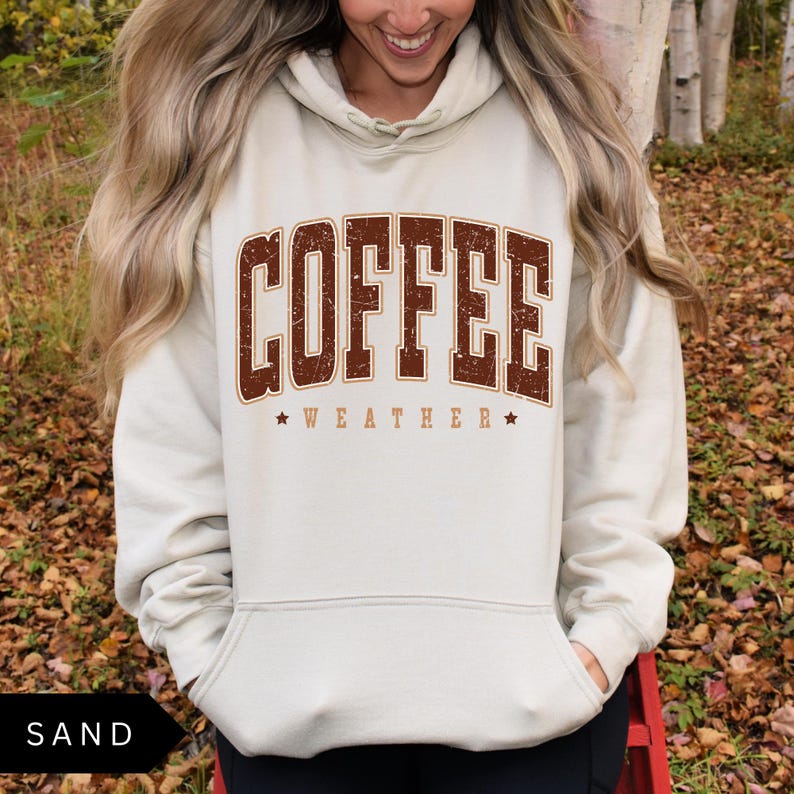 Puede incluir: Una sudadera con capucha beige claro con un gr&aacute;fico vintage marr&oacute;n que dice "COFFEE WEATHER" en may&uacute;sculas.