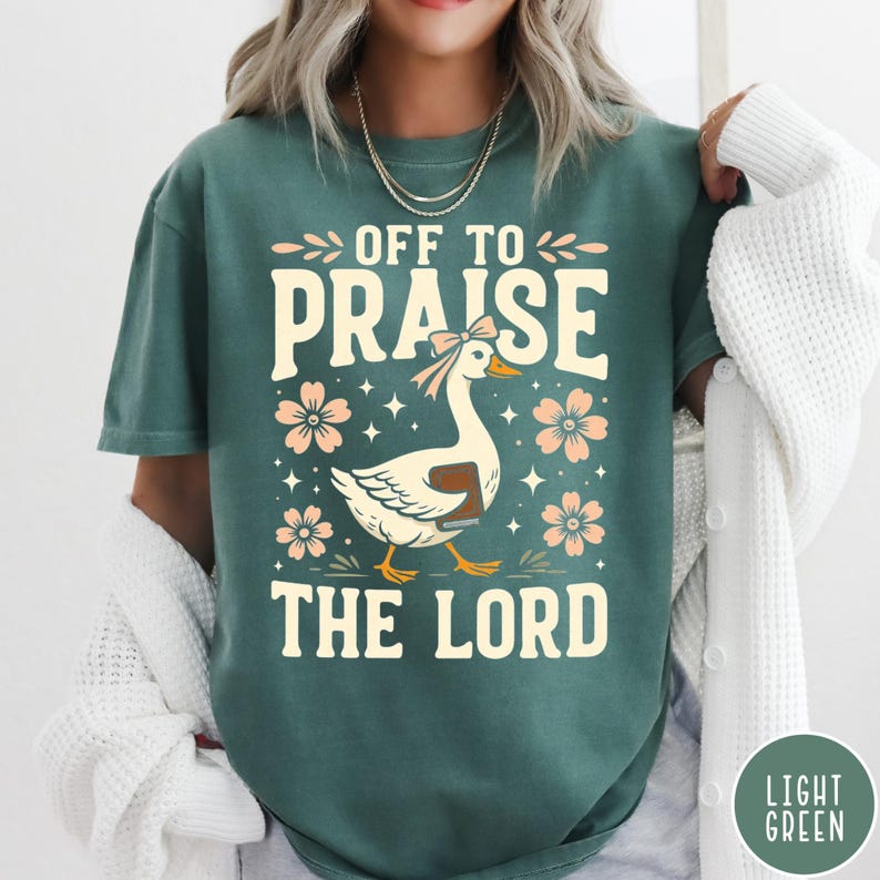 Puede incluir: Camiseta verde claro con el texto "OFF TO PRAISE THE LORD" en una fuente caprichosa. El dise&ntilde;o incluye un ganso de dibujos animados con un lazo y un libro, rodeado de flores y estrellas. La camiseta es de color liso.
