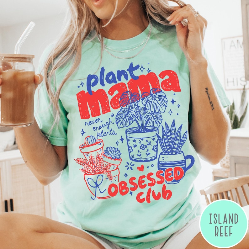 Puede incluir: Camiseta verde claro con las palabras "plant mama" en rojo y azul, junto con ilustraciones de plantas en macetas. La camiseta tambi&eacute;n presenta el texto "never enough plants" y "obsessed club".