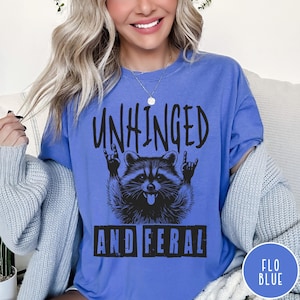 May include: A blue t-shirt with a black graphic of a raccoon with the text "Unhinged and Feral" printed on it.