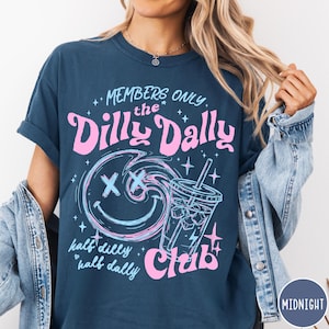May include: Navy blue t-shirt with a graphic design. The design features the text "MEMBERS ONLY the Dilly Dally Club" in pink and blue, along with a smiley face and a drink. The words "half dilly half dally" are also included.