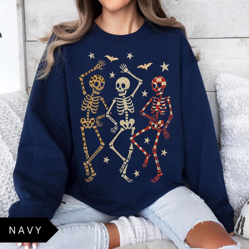 Puede incluir: Sudadera azul marino con tres esqueletos bailando en dorado y rojo, con estrellas y murci&eacute;lagos. La palabra "NAVY" est&aacute; en la parte inferior. Un dise&ntilde;o divertido y festivo para Halloween.