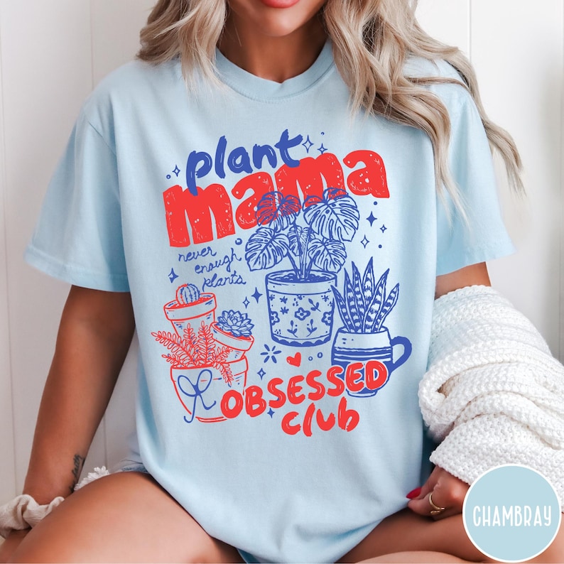 Puede incluir: Camiseta azul claro con las palabras "Plant Mama" en rojo y azul, junto con la frase "never enough plants". La camiseta presenta ilustraciones de plantas en macetas y las palabras "Obsessed Club" en rojo.