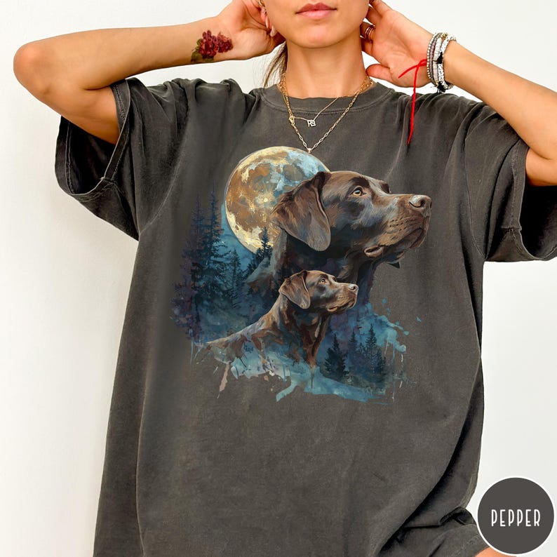 May include: Dark grey t-shirt featuring a watercolor illustration of two Labrador Retrievers with a full moon and forest backdrop. The design includes shades of brown, blue, and white.