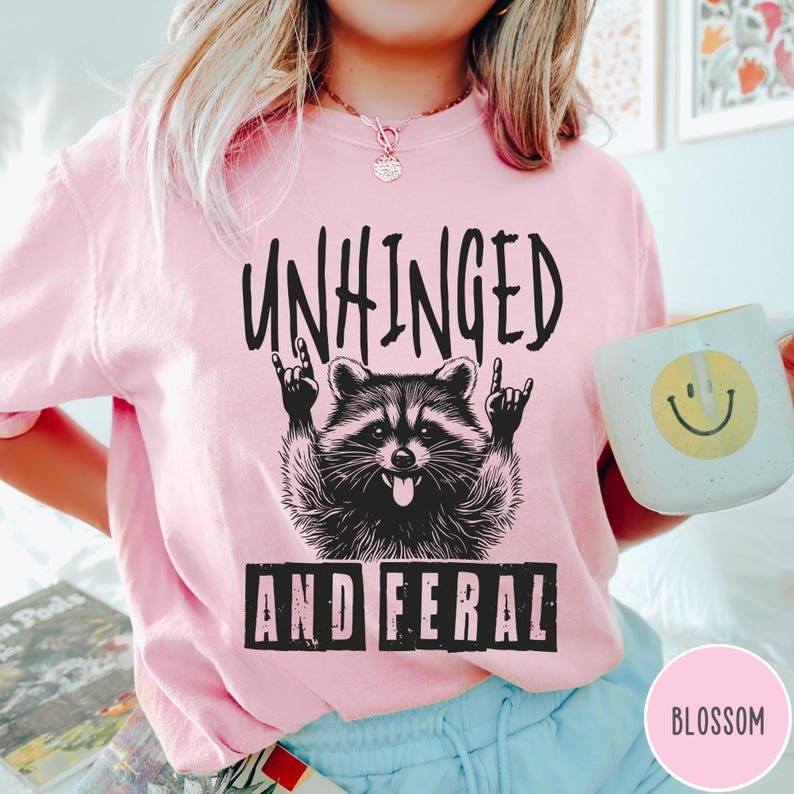 May include: Pink t-shirt with a black and white illustration of a raccoon with the text "Unhinged and Feral" printed on it.