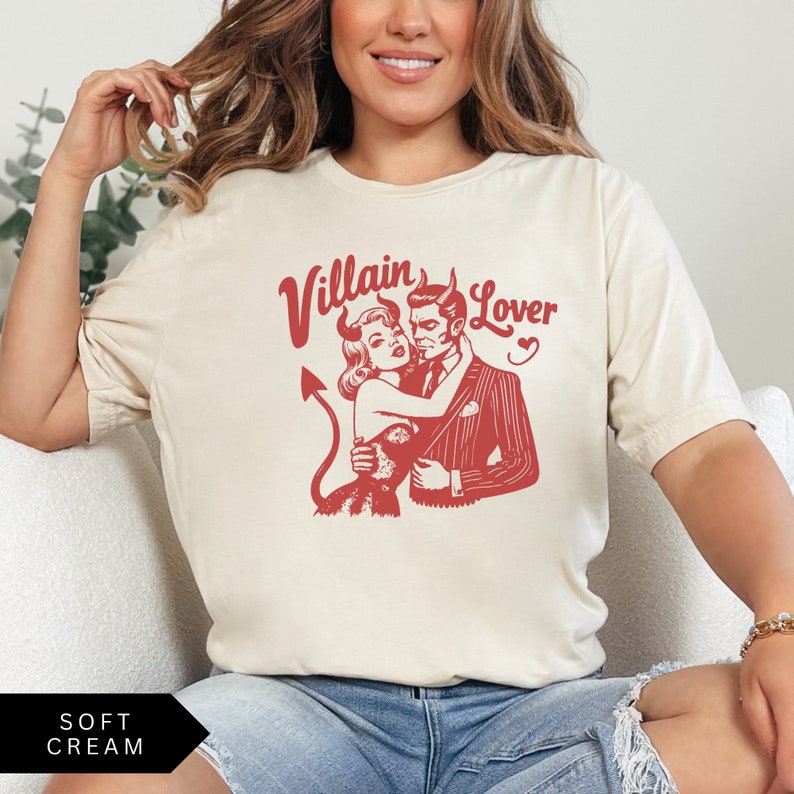 May include: A cream colored t-shirt with a red graphic of a couple in a vintage style. The text "Villain Lover" is printed in red above the couple.