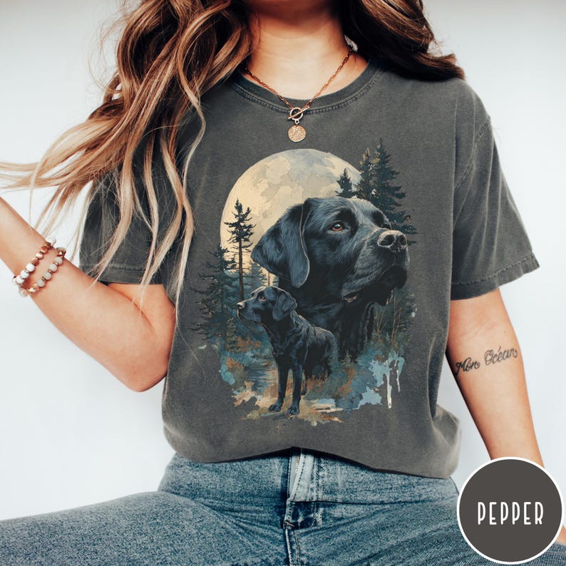 May include: Dark grey t-shirt featuring a graphic of a black Labrador Retriever with a full moon and forest background. The design includes two images of the dog, one larger and one smaller, with a nature scene.