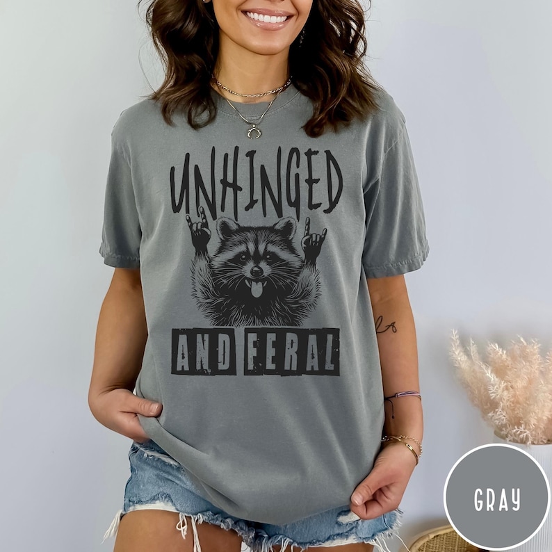 May include: Gray t-shirt with a black graphic of a raccoon with the text "Unhinged and Feral" on it.