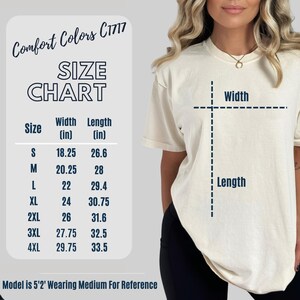 Puede incluir: Tabla de tallas para una camiseta con medidas en pulgadas. La tabla muestra el ancho y la longitud de la camiseta en las tallas S, M, L, XL, 2XL, 3XL y 4XL. La modelo lleva una talla M.