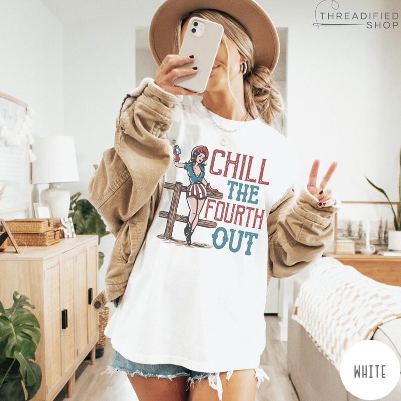 May include: White t-shirt with the text "CHILL THE FOURTH OUT" and a vintage-style illustration of a woman in patriotic attire. The design features red, white, and blue colors, perfect for celebrating Independence Day.