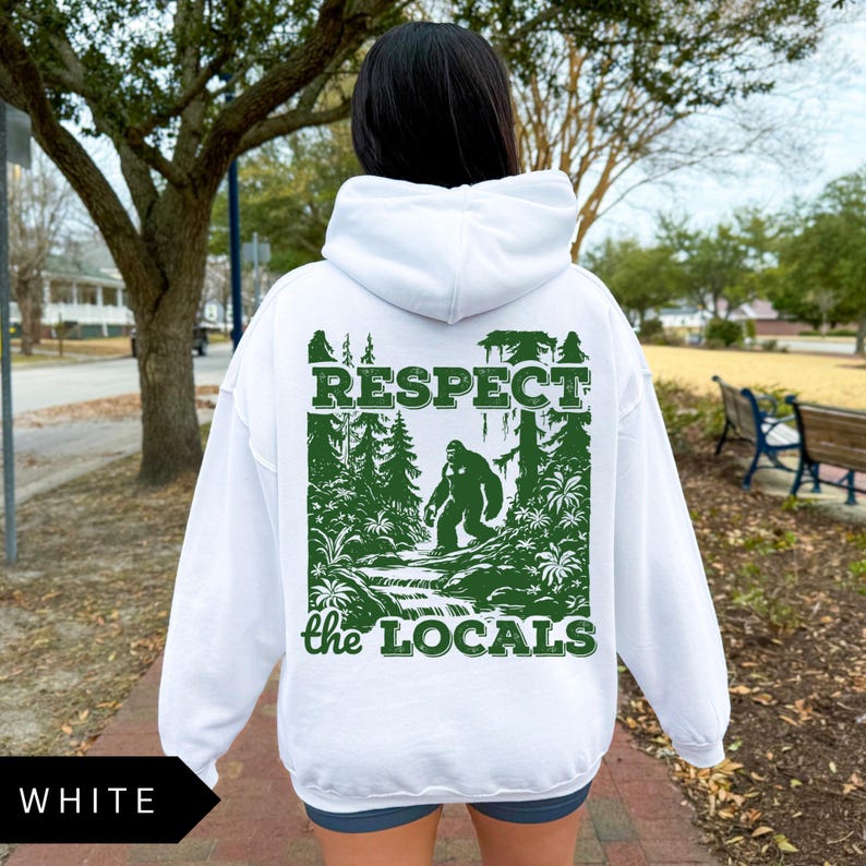 May include: White hoodie with a green graphic print of a Bigfoot walking through a forest. The graphic says "Respect the Locals".