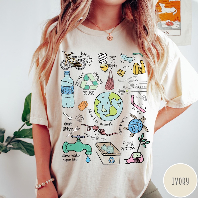 May include: A cream coloured t-shirt with a colourful graphic design featuring illustrations of ways to help the environment. The graphic includes a bicycle, a lightbulb, a water tap, a plant, a turtle, a recycling symbol, and the words "bike more, drive less", "turn off lights", "save the planet", "save a turtle", "plant a tree", "save water, save life", "don't litter", "unplug things", "skip a straw", "volunteer", "recycle", "reduce", "reuse", and "being plastic".