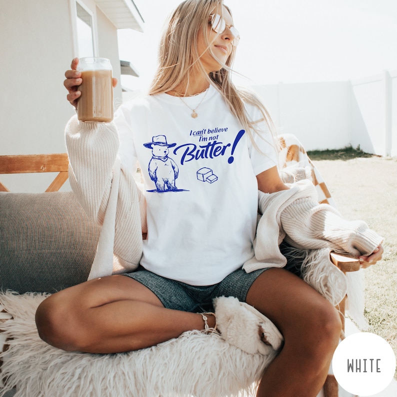 May include: White t-shirt with a cartoon bear wearing a hat and the text "I can't believe I'm not Butter!" in blue.