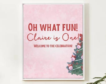 Könnte beinhalten: Gerahmter rosa Druck mit dem Text „OH WHAT FUN! Claire is One! Welcome to the Celebration!“. Eine Weihnachtsbaum-Illustration mit Ornamenten und Schleifen befindet sich in der unteren rechten Ecke. Der Druck ist in einem weißen Rahmen.