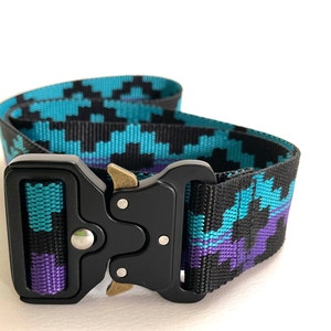 Peut inclure: Une ceinture à motif noir et bleu avec une boucle en métal noir. La boucle a un bouton de déverrouillage argenté et un curseur en laiton.