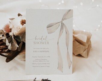 Könnte beinhalten: Eine Einladungskarte zur Brautparty mit einem Aquarell-Schleifendesign in neutralen Tönen. Die Karte zeigt die Worte "bridal shower" in eleganter Schrift sowie Details zur Veranstaltung. Die Einladung befindet sich vor einem weichen, verschwommenen Hintergrund.