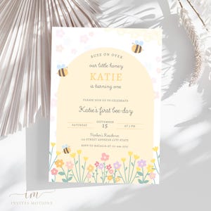 May include: A yellow and white bee-themed first birthday party invitation with a cartoon bee and flowers. The invitation says "Buzz on over our little honey Katie is turning one. Please join us to celebrate Katie's first bee-day. Saturday, September 15 at 5 PM. Parker's Residence 123 Street Address City State. RSVP to Natalia at 111-444-5555."