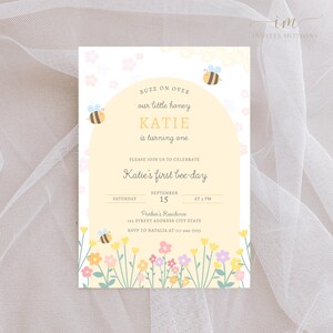 May include: A yellow and white bee-themed first birthday party invitation with a bee illustration and the text "Buzz on over our little honey Katie is turning one. Please join us to celebrate Katie's first bee-day. Saturday September 15 at 3 PM. Parker's Residence 123 Street Address City State RSVP to Natalia at 111-444-5555."