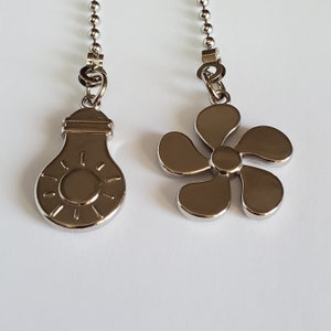 Puede incluir: Dos cadenas de tirador de ventilador de techo plateadas. Una cadena tiene un dije en forma de bombilla con un diseño de sol. La otra cadena tiene un dije en forma de estrella de cinco puntas.