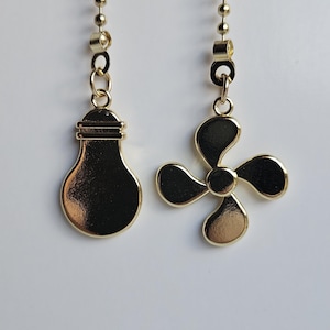 Puede incluir: Dos cadenas doradas para ventilador de techo y luz. Una tiene un dije de bombilla y la otra un dije de aspa de ventilador. Ambos dijes cuelgan de una cadena dorada de cuentas.