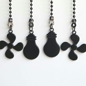 May include: Four black ceiling fan and light pull chain accessories hanging against a white background. Two are fan blade shapes, and two are light bulb shapes. Each is attached to a black beaded chain.