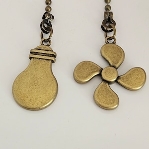 May include: Two gold-toned metal fan pull chains. One chain has a light bulb charm and the other has a four-blade fan charm.