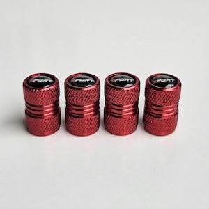 May include: Four red tire valve stem caps with a textured design. Each cap has a black top with the word "SPORT" in white. The caps are cylindrical and appear to be made of metal.