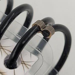 May include: Close-up of a black metal binder coil with a silver metal binding clip. The clip is shaped like a heart.