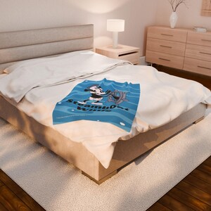 May include: A blue blanket featuring a cartoon image of a character at the helm of a ship, with the words "Steamboat Willie" in white. The blanket is on a bed with a white comforter.