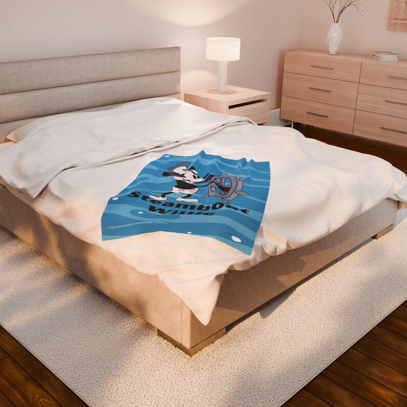 May include: A blue blanket featuring a cartoon image of a character at the helm of a ship, with the words "Steamboat Willie" in white. The blanket is on a bed with a white comforter.