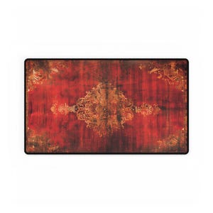 May include: A rectangular red and brown decorative mat with an ornate, golden-colored central design. The mat has a distressed, vintage appearance, with darker edges and a black border. The design features floral and scrollwork patterns.