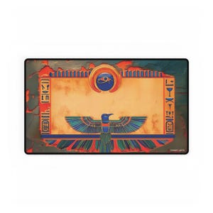 Puede incluir: Un tapete de juego rectangular con diseño egipcio, un campo central beige, un símbolo del Ojo de Horus azul y un ave estilizada con las alas extendidas. El borde incluye iconos tipo jeroglífico y el texto COMBAT MATS.